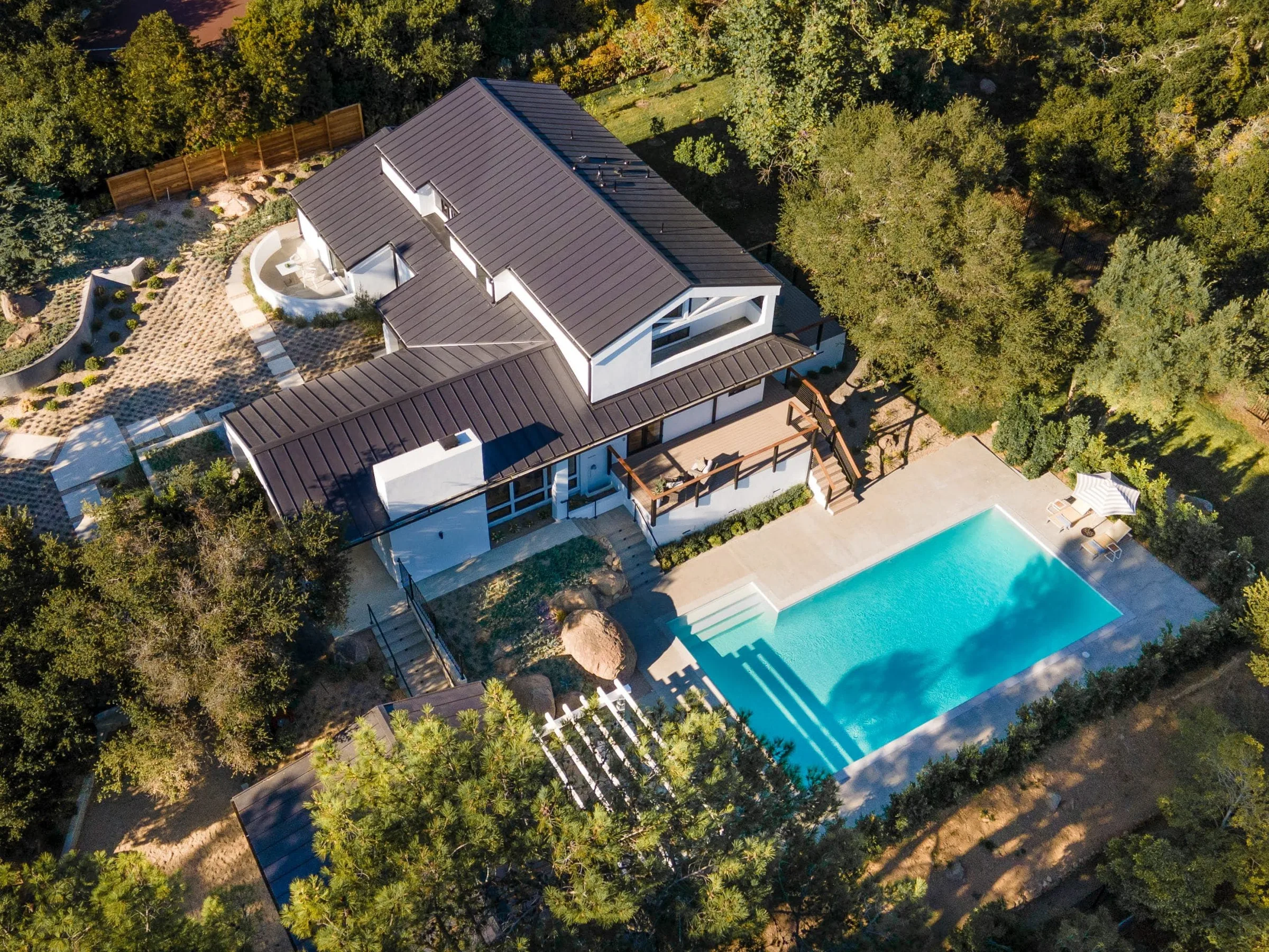 Top-down aerial of a modern home with a pool set into wooded grounds
