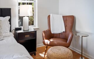 A cozy bedroom corner with a leather chair and side table, captured by professional photography for real estate drone tours.