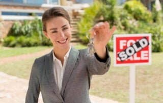 Real estate agent holding keys with SOLD sign, property showcased through innovative drone photography and virtual tour technology.