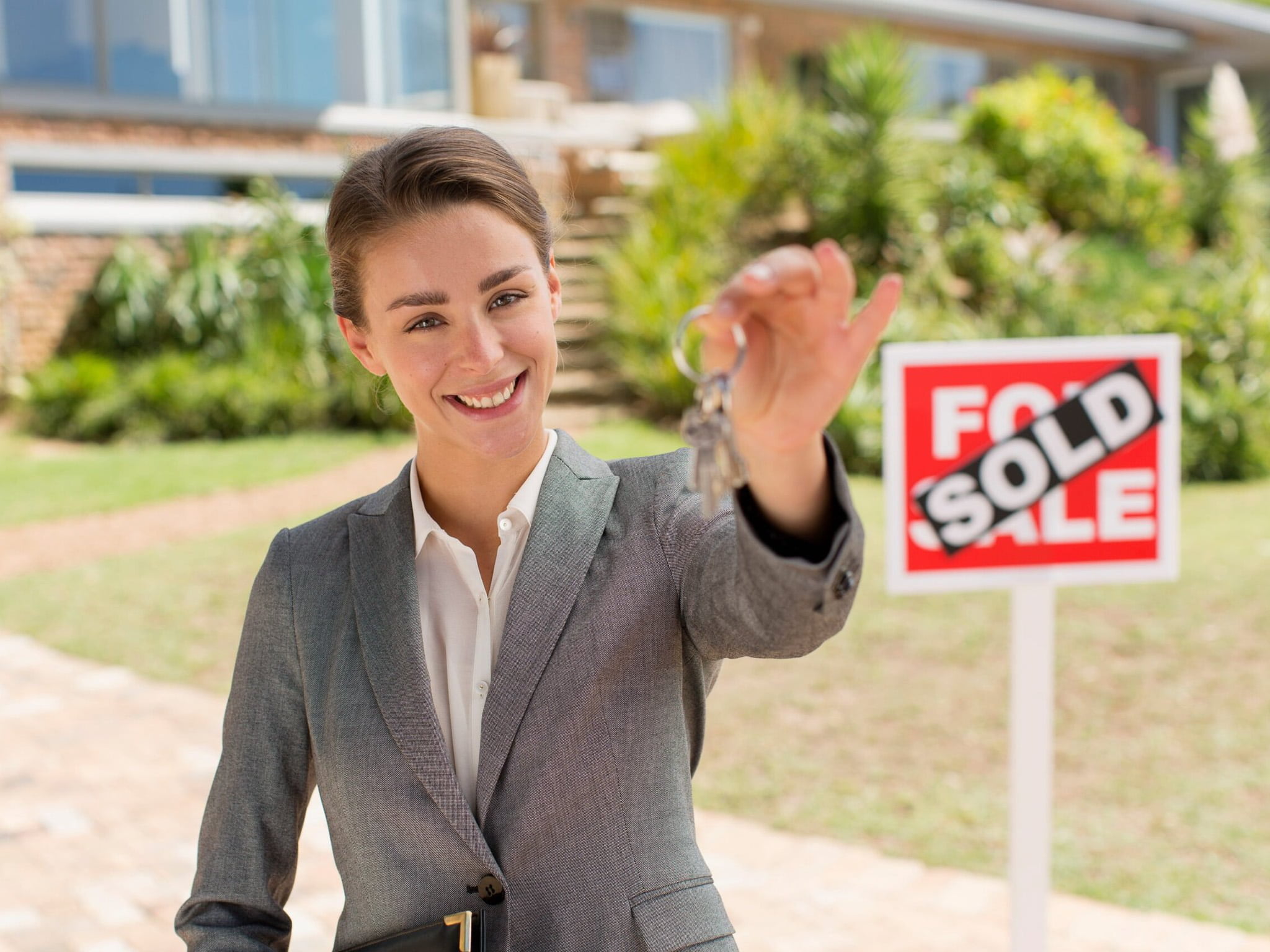 Real estate agent holding keys with SOLD sign, property showcased through innovative drone photography and virtual tour technology.