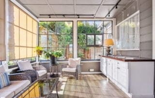 Sunlit-interior-of-a-home-showing-a-modern-design-with-wicker-furniture-and-large-windows-overlooking-a-garden-representing-real-estate-marketing-enhanced-by-drone-flights-and-FPV-drone-shots.